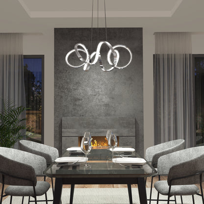 A modern dining room featuring a glass table for four, gray upholstered chairs, Artika’s Swirl Ribbon LED pendant light, a textured gray wall, fireplace, floor-to-ceiling windows with sheer curtains, and a potted plant.