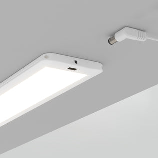 The Artika Maestro under cabinet LED light 3CCT is a rectangular white fixture mounted beneath a gray surface, with its power cable and connector plugged in.