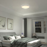 Modern bedroom with a gray bed, green comforter, wall art above the headboard, a window with curtains, a cushioned window seat, and a round ceiling light illuminating the room.