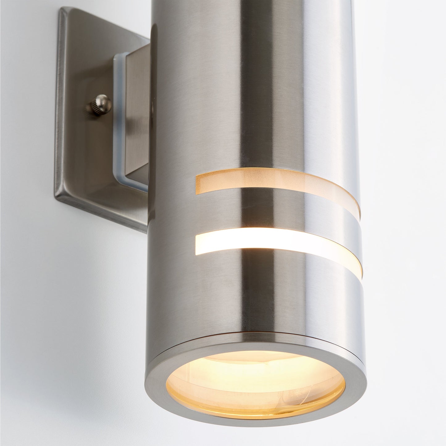 The Voltz indoor/outdoor wall light by Artika-CAN-dev features a modern brushed metal design with a cylindrical shape, two horizontal cutouts, frosted glass bottom, rust-resistant finish, and mounts on a rectangular backplate.