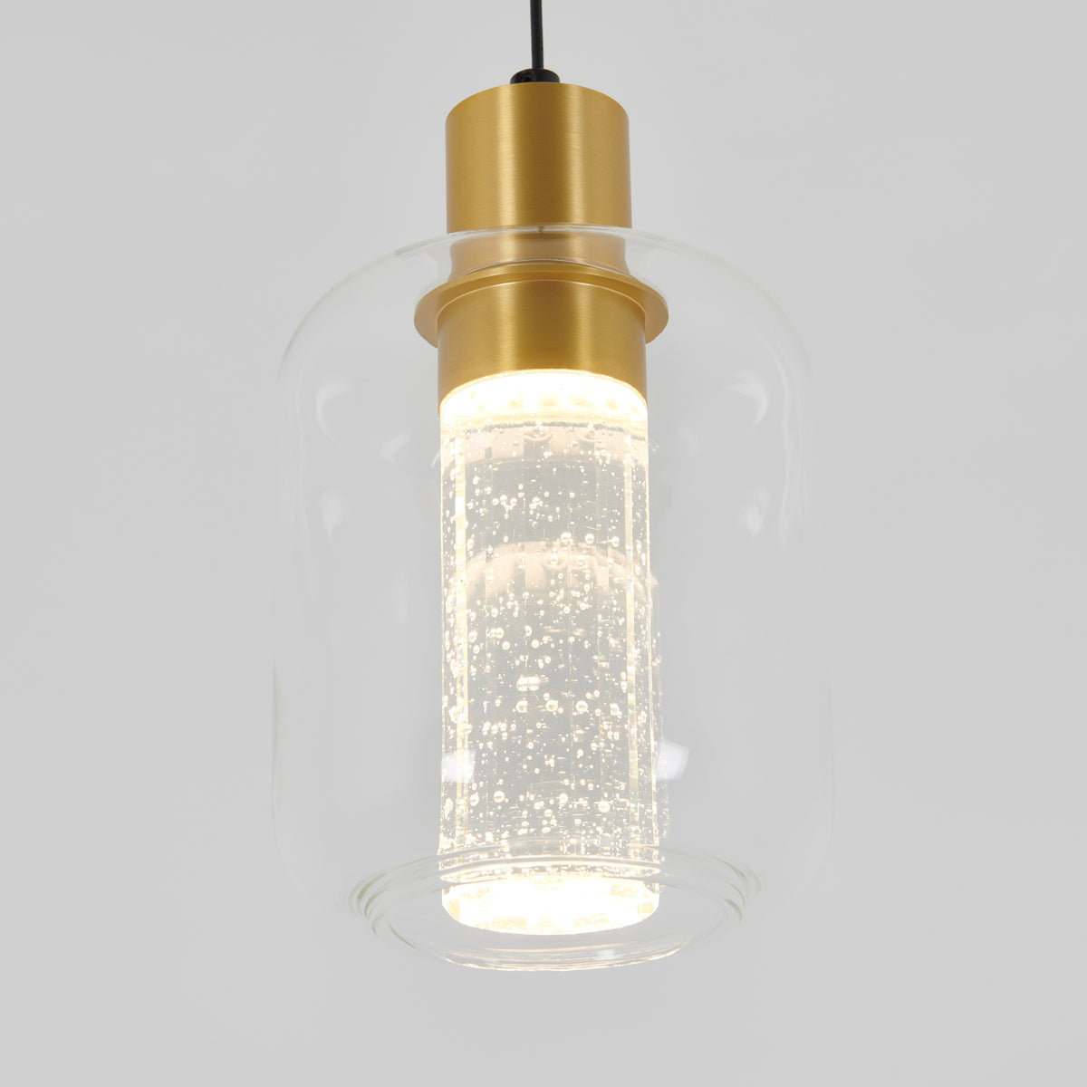The Artika Champagne Globe modern LED pendant light features a clear glass shade with small bubbles, a cylindrical gold fixture, and a glowing light inside.