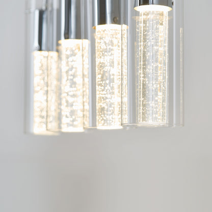 Close-up of the Artika Bubble Flow 4-light pendant, featuring modern cylindrical glass shades with bubbles inside, emitting a bright white glow against a plain light background.