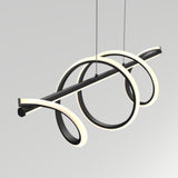 A modern, sculptural pendant light fixture with two glowing circular LED loops intertwined around a horizontal black rod, suspended by thin cables against a plain, light gray background.