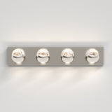 A modern wall-mounted light fixture with a rectangular metallic base and four evenly spaced round glass bulb covers, each emitting light, against a plain light-colored wall.