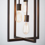 Close-up of a modern light fixture with three exposed Edison-style bulbs suspended inside a rectangular metal frame. The bulbs emit a warm glow against a plain, light background.