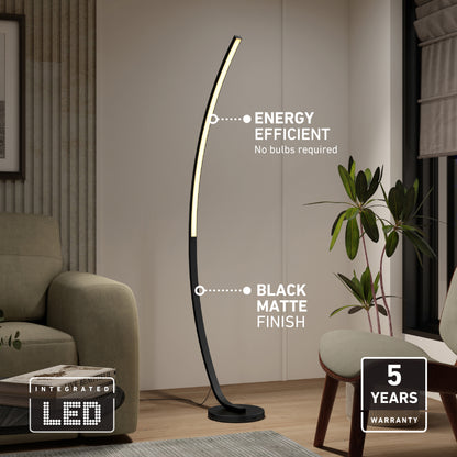 The Arc LED Floor Lamp by Artika, featuring a modern arched design and sleek black matte finish, stands in a living room. Labels note energy efficiency, dimmable integrated LED (no bulbs needed), and a 5-year warranty. A plant and curtain appear behind it.