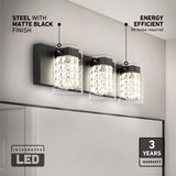 A modern wall light fixture with three crystal-like LED lights in a matte black finish, mounted above a mirror in a bathroom. Labels highlight its integrated LED, energy efficiency, and 3-year warranty.