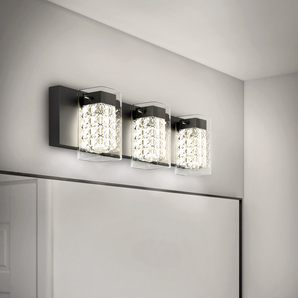 A modern bathroom wall light fixture with three square, crystal-like glass shades mounted on a rectangular black base, installed above a large mirror on a light gray wall.