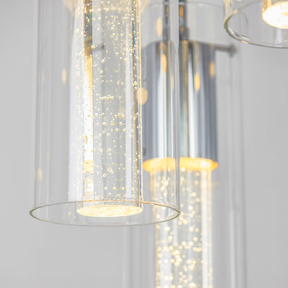 Close-up of the Artika Essence 5-light LED pendant, showcasing cylindrical glass shades with bubble-like details, softly illuminated against a light background.