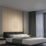 A modern bedroom with a gray bed, white and gray bedding, a textured beige accent wall behind the bed, dark curtains, a large window, and a small nightstand with a plant.