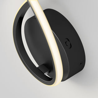 A close-up of the Artika Gamma modern LED wall sconce 5 CCT, featuring a circular black design with a glowing LED strip around its edge, mounted on a white wall.