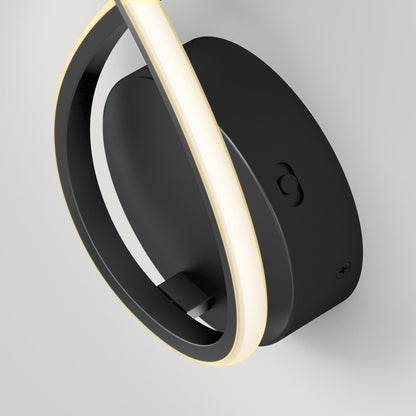 A close-up of the Artika Gamma modern LED wall sconce 5 CCT, featuring a circular black design with a glowing LED strip around its edge, mounted on a white wall.