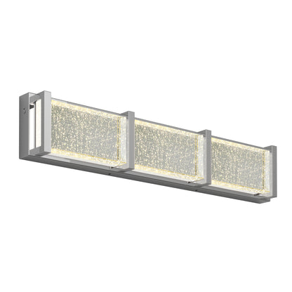 The Artika Subway Essence 3 LED bathroom vanity light features three glass-like panels with embedded bubbles, framed in silver metal. Wall-mounted, it illuminates your space with a sparkling effect for a modern look.