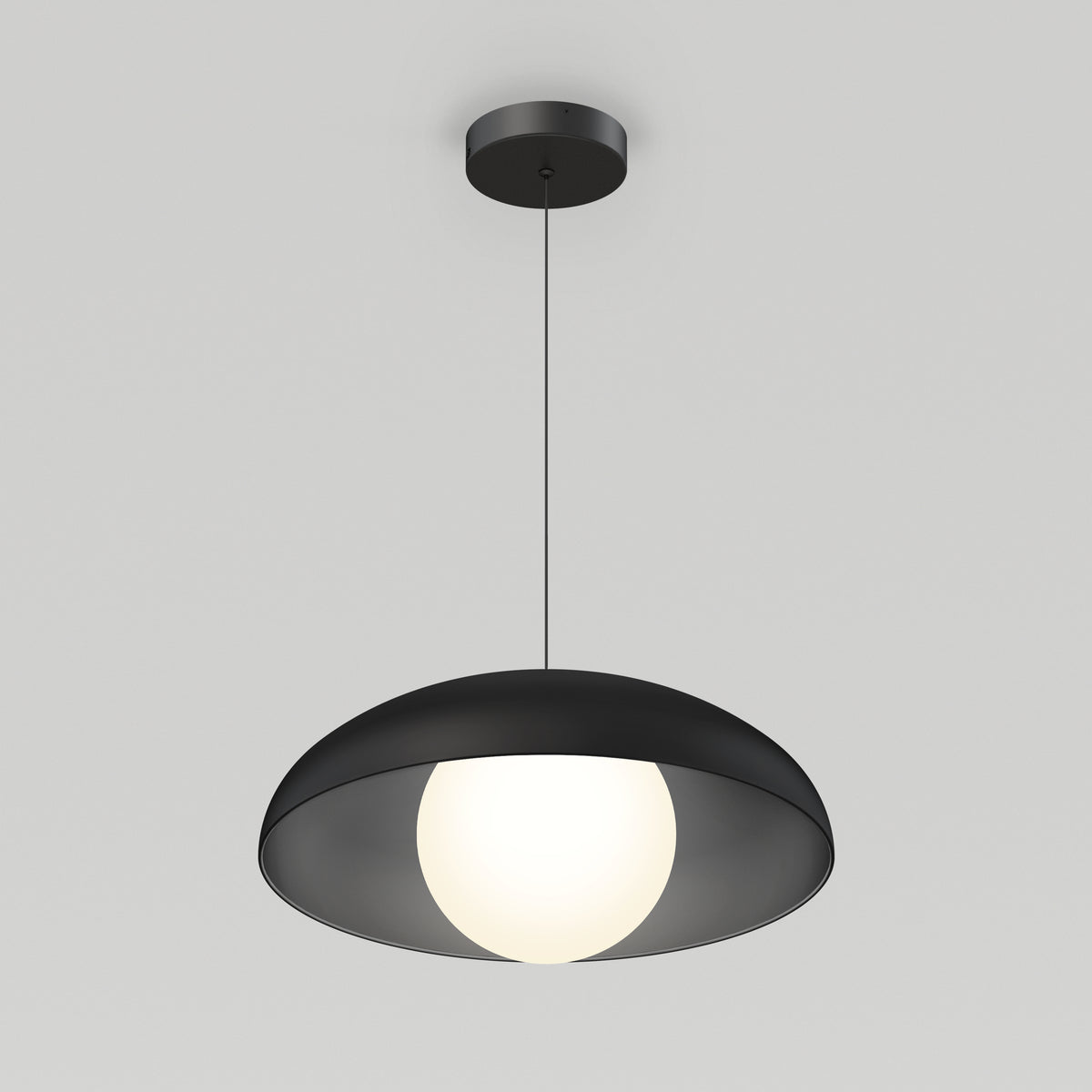 A modern black pendant light with a wide, shallow shade hangs from the ceiling, featuring a glowing white spherical bulb at its center against a plain light gray background.