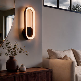 An oval-shaped Aiden modern LED indoor-outdoor wall light 5 CCT emitting a warm glow, mounted above a wooden console table.