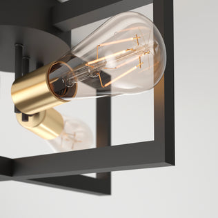 Close-up of the Artika Holt 3-light flush mount light, showcasing exposed Edison bulbs with visible filaments in gold sockets, set within a black geometric metal frame against a plain white background.