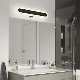 A modern bathroom features a large mirror, rectangular sink, soap dispensers, two small plants, and the Artika Pista modern LED bathroom vanity light 5 CCT above the mirror. To the right is a glass shower with dark tile.