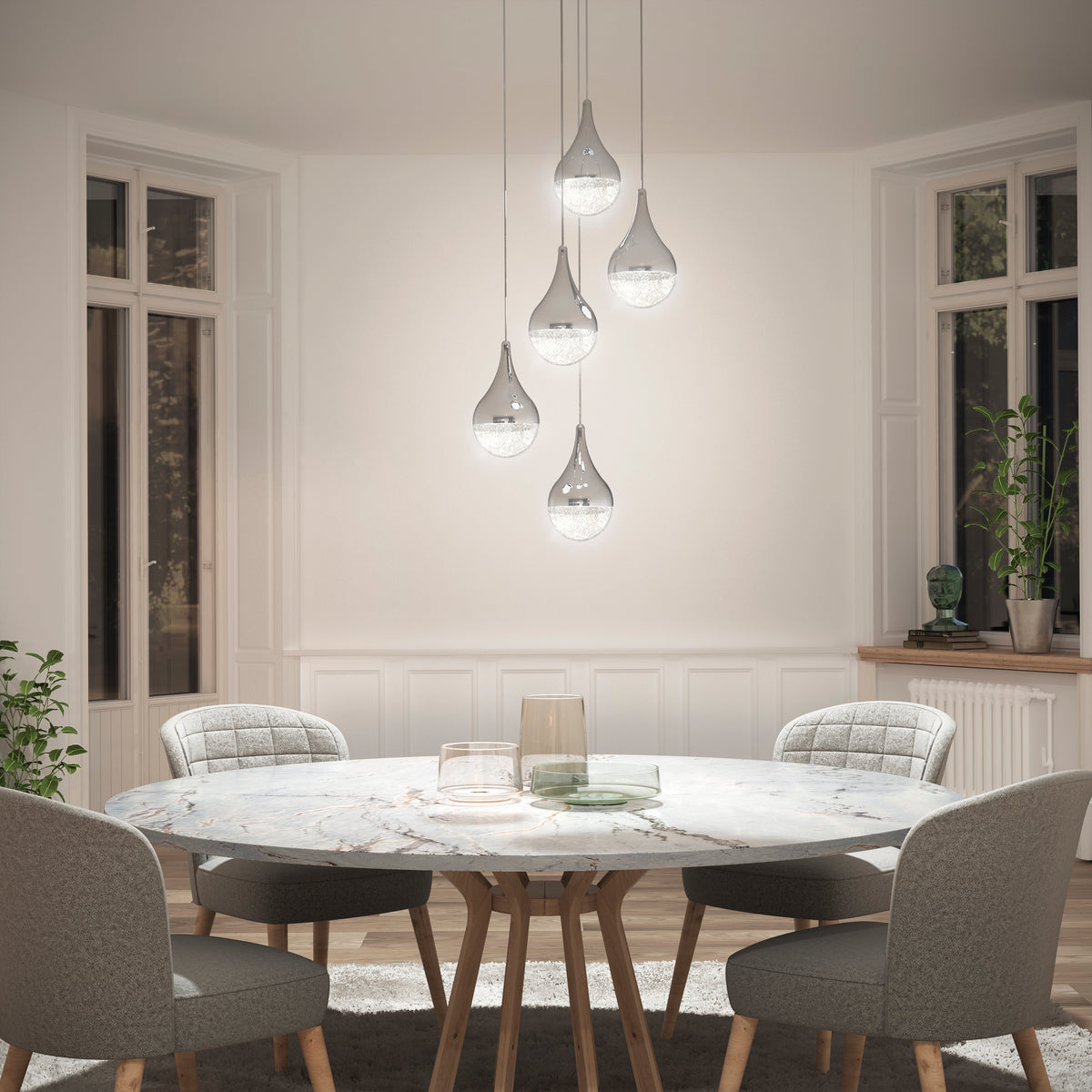 A bright, elegant dining area features a round marble table, four upholstered chairs, and the Artika Glitzer 5-light LED pendant hanging above large windows with minimal decor.