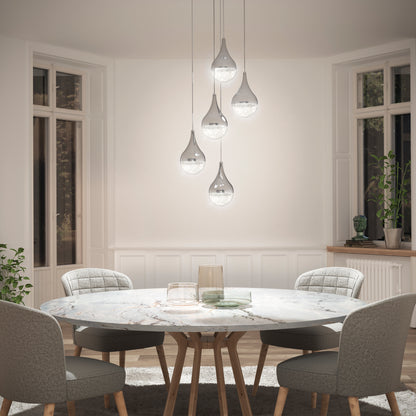 A bright, elegant dining area features a round marble table, four upholstered chairs, and the Artika Glitzer 5-light LED pendant hanging above large windows with minimal decor.