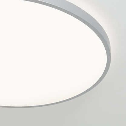 A close-up of the Artika Jupiter 23 in. LED flush mount light, featuring a white glowing surface and slim gray frame, ceiling-mounted and seen from below; includes remote control.