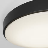 Close-up of a modern, round ceiling light fixture with a black rim and a white, glowing diffuser against a light gray background.