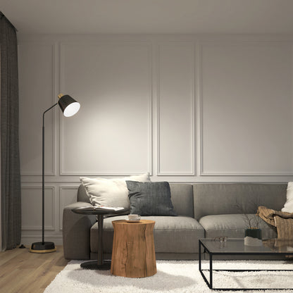 A modern living room features a gray sofa with assorted cushions, a glass coffee table, a tree stump side table with a cup, and the Artika Alton LED modern floor lamp on wooden flooring with a white rug and paneled white walls.