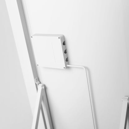 A close-up of the Artika Emeraude Full Length Mirror mounted on a white wall, with a white cable extending downward. The minimal all-white background highlights the mirror’s sleek design.