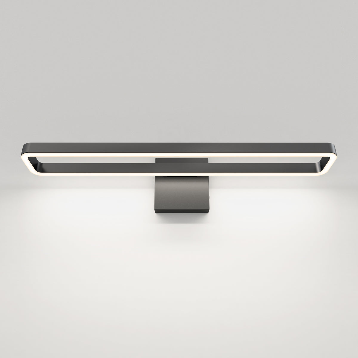 A modern black wall-mounted LED light fixture with a rectangular frame emits a soft white glow, illuminating the wall below against a plain white background.