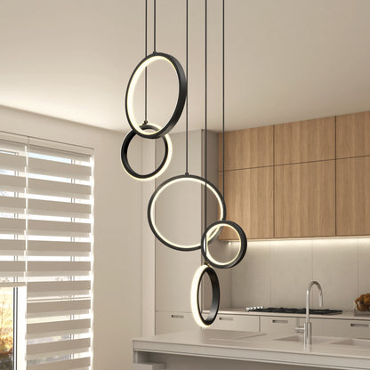 Modern kitchen with wood cabinets and white countertops, featuring the Artika Elmo 5-light LED pendant 5 CCT’s sleek overlapping black rings above the island. Sunlight streams through horizontal blinds on the window.