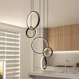 Modern kitchen with light wood cabinets, a white countertop, and a set of four black circular pendant lights hanging at different heights above an island. Window with horizontal blinds lets in natural light.