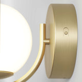 A close-up of a modern wall sconce with a round, frosted glass lampshade and a brushed gold mounting plate featuring a small round button.