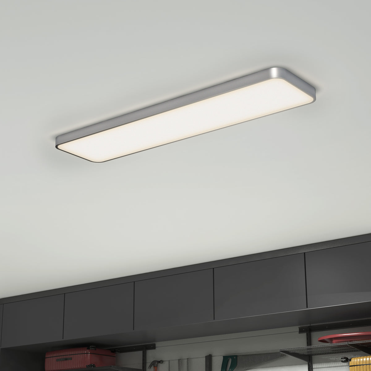 A modern rectangular ceiling light with a silver frame is illuminated above dark gray cabinets in a room, giving off a bright, even light.