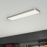 A modern rectangular ceiling light with a silver frame is illuminated above dark gray cabinets in a room, giving off a bright, even light.