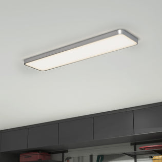 The Artika Europa 48 LED flush mount light, featuring a silver frame and remote control, is illuminated on a white ceiling above dark cabinets, adding a modern touch to the contemporary workspace.