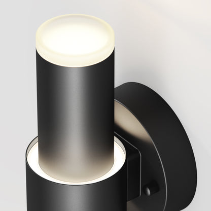 The Artika Dani modern LED indoor-outdoor wall light 5 CCT is a black, cylindrical fixture with illuminated top and bottom sections, mounted on a round base against a light-colored wall.