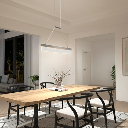 A minimalist, neutral-toned dining room features a wooden table, four black chairs, a vase with branches, and large windows. Above the table hangs Artika’s Essence Bar LED pendant light for modern illumination.