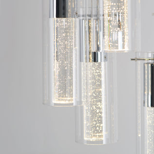 The Artika Bubble Swirl 5-light pendant features modern cylindrical lights with clear, bubble-filled glass and chrome accents, softly illuminated against a plain light gray background.