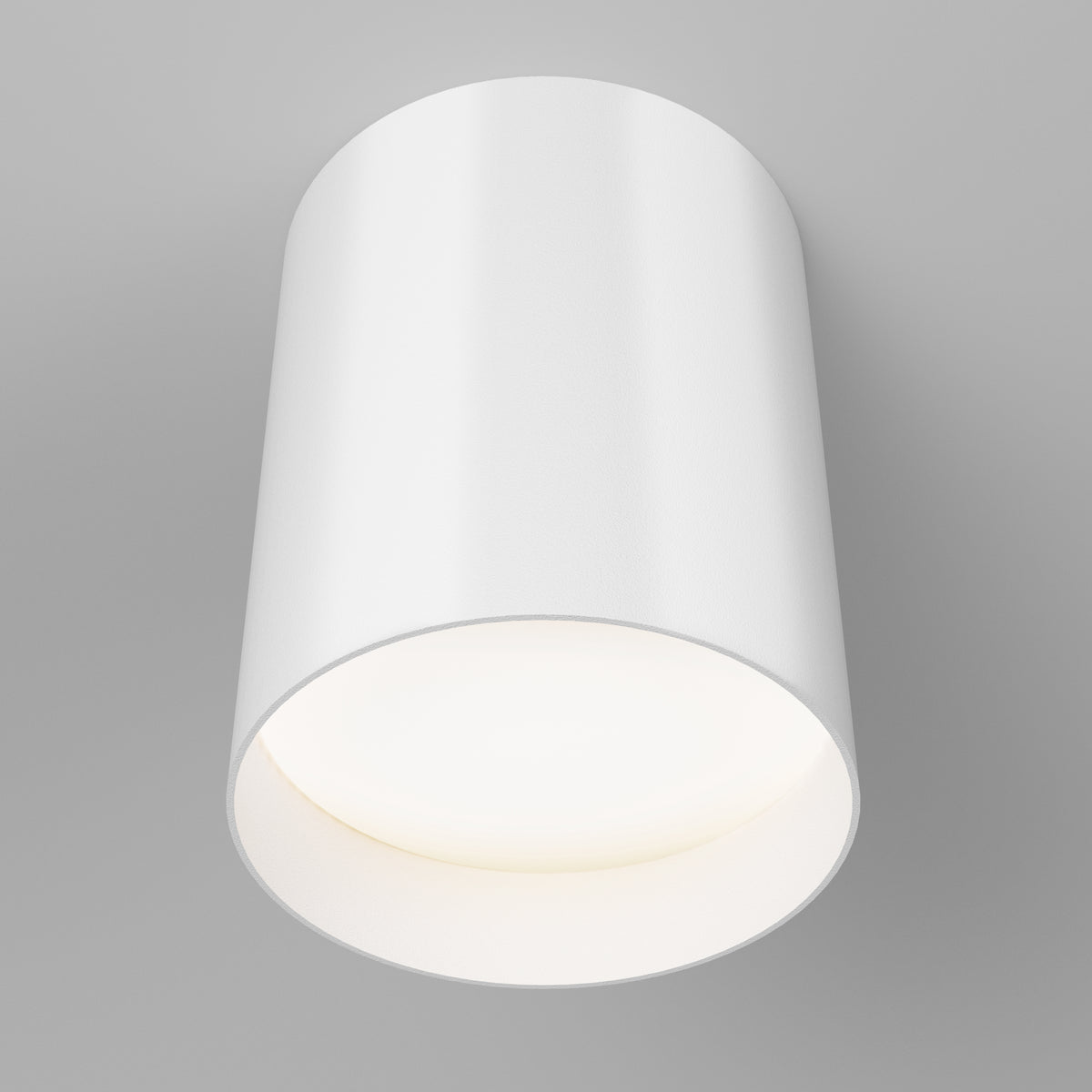 A modern, cylindrical white ceiling light fixture is mounted on a light gray ceiling, emitting a soft, even glow downward.
