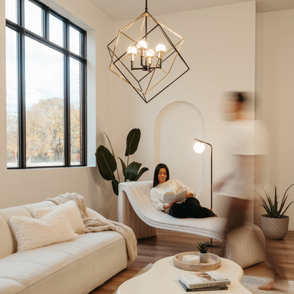 A modern living room with large windows features the Artika Peyton LED modern mid-century pendant light, neutral furnishings, and cozy decor. A woman reads on a chaise lounge as a blurred figure walks by, with plants adding warmth to the space.