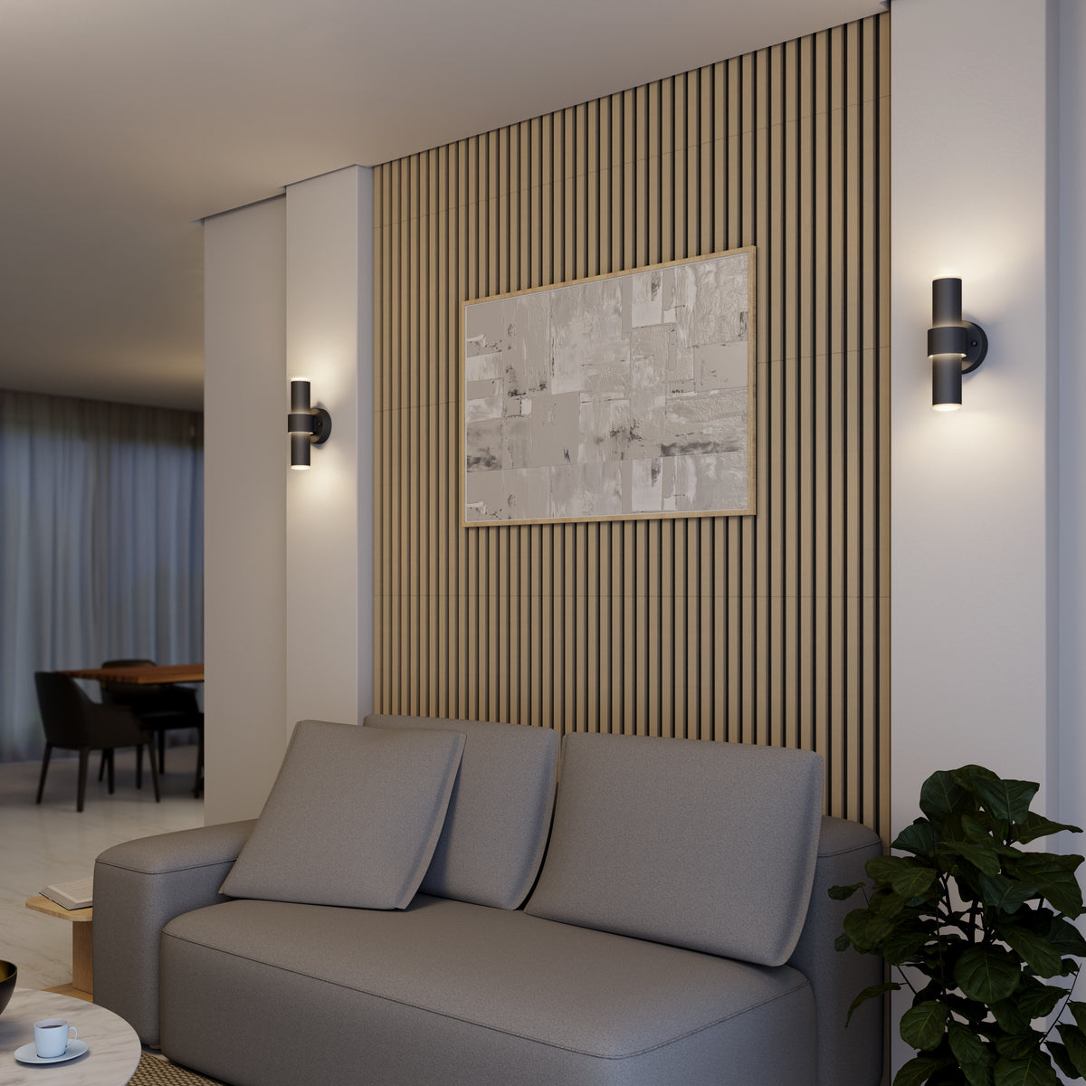 Modern living room with a grey sofa, a wooden slatted accent wall, abstract artwork, two wall sconces, and a leafy green plant in the corner. The space is softly lit and opens to a dining area in the background.