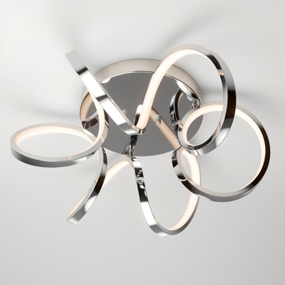 The Artika Swirl Ribbon flush mount light features intertwined metallic arms with built-in LED strips on a round chrome base, providing soft, diffused light to any white ceiling.