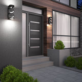 Modern house entrance with gray double doors, horizontal glass panels, and contemporary wall lights. Steps lead up to the doorway, and neatly trimmed bushes are planted in front and beside the entrance.