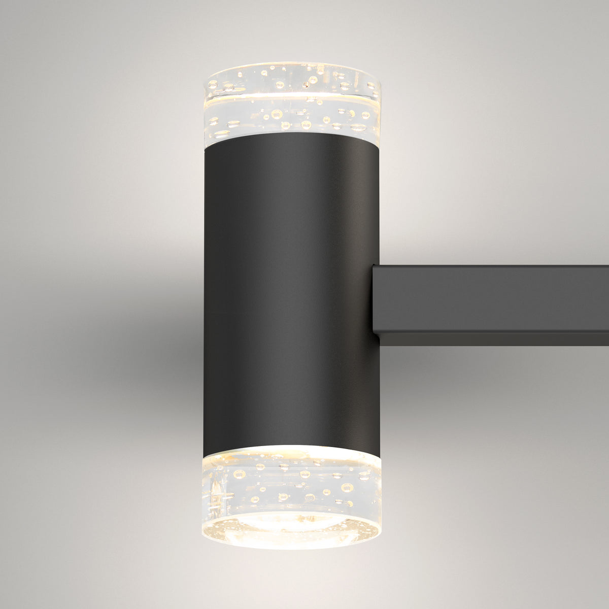 A modern wall-mounted black sconce light with cylindrical frosted glass ends featuring bubble-like patterns, illuminating both upward and downward against a plain light-colored wall.