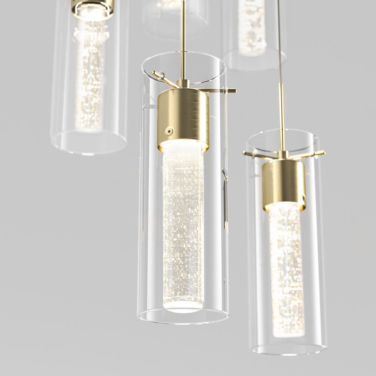 Close-up view of modern pendant lights with cylindrical glass shades and gold-colored fixtures, featuring inner tubes filled with sparkling bubbles, suspended against a plain light background.