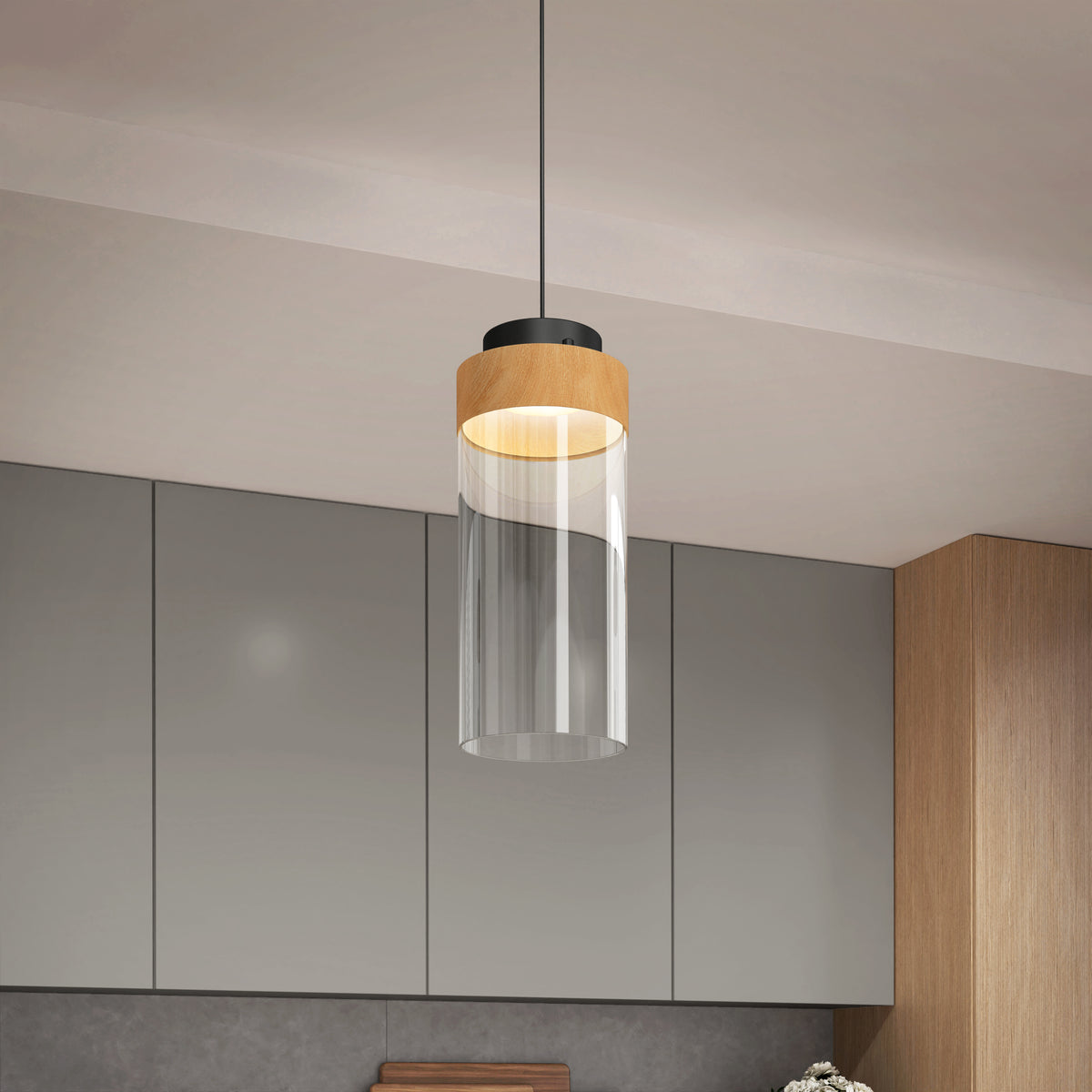A modern pendant light with a cylindrical glass shade and a wooden accent hangs from the ceiling in a contemporary kitchen with gray cabinets and wood details.