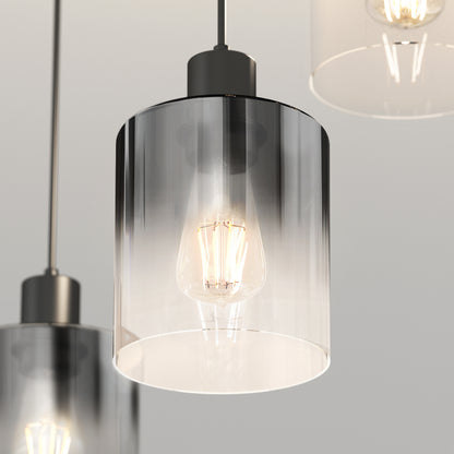 A close-up of the Artika Haze modern 3-light pendant, featuring cylindrical transparent glass shades and visible glowing filament bulbs, suspended from the ceiling with two other lights partially shown in the background.