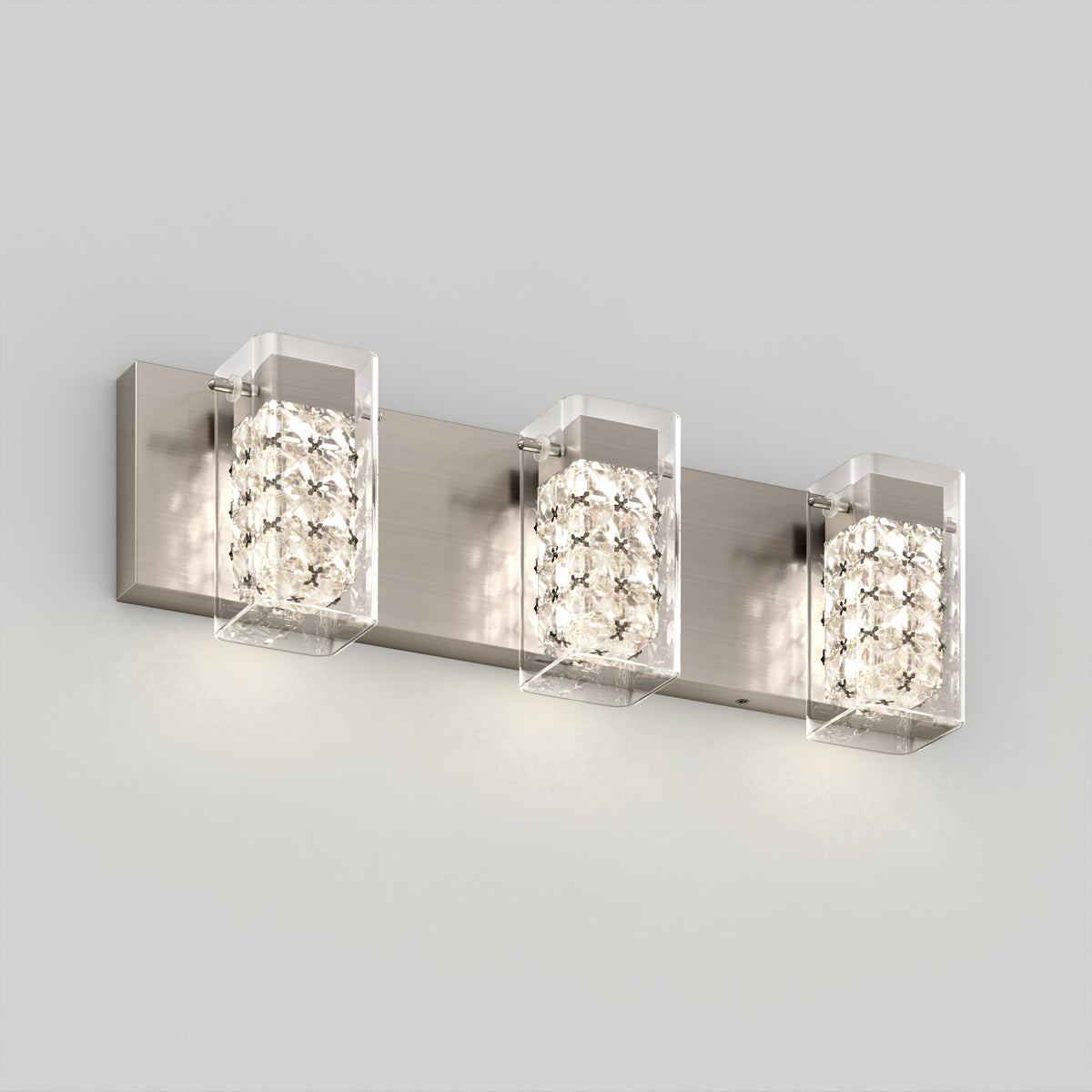 The Artika Crystal Cube LED bathroom vanity light 5 CCT features three cube-shaped lights with clear crystal accents and a brushed metal base, mounted on a plain light gray wall.