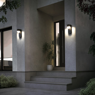 At dusk, a modern house entrance features a black door, potted plant, and two Artika Bloom indoor-outdoor LED wall lights (3 CCT) mounted on the wall, illuminating the porch and steps.