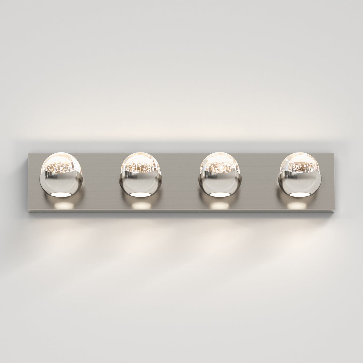 A modern wall-mounted light fixture with four round, chrome-finished bulbs evenly spaced on a rectangular metal base, casting light against a white wall.
