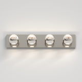 A modern wall-mounted light fixture with four round, chrome-finished bulbs evenly spaced on a rectangular metal base, casting light against a white wall.